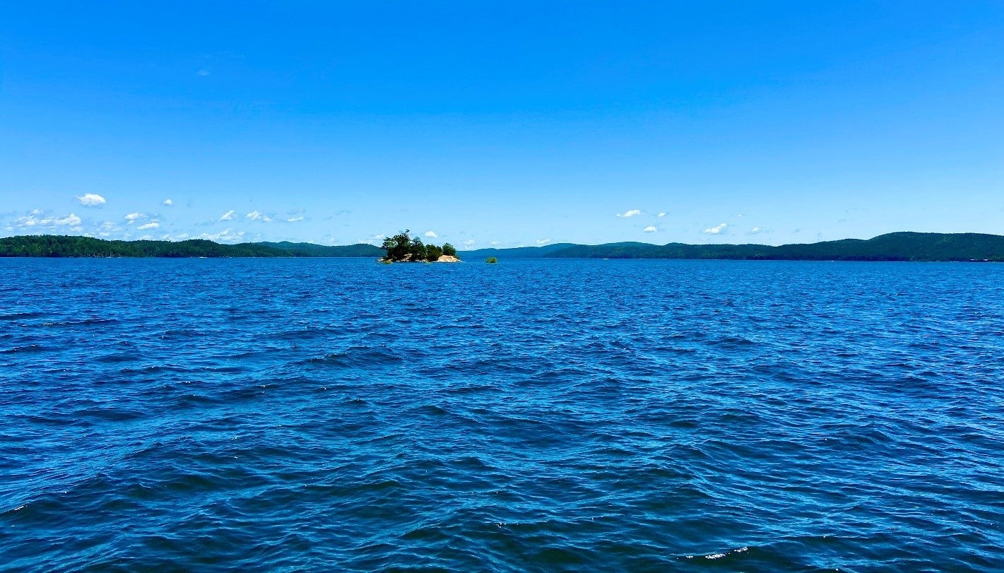 A small island covered in pine trees sits in the middle of a large lake surrounded by mountains. 